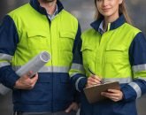 Two site engineers in yellow and navy hi-vis jackets with white hard hats